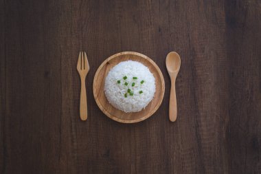 Ahşap bir tabakta, üzerinde yeşil soğan dilimlenmiş tahta kaşıkla, ahşap bir masada ahşap çatalla pişirilmiş beyaz pirinç. Tayland Jasmine pirinci..