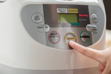 Yasemin pilavı pişirmek için kadın eli yasemin menüsüne bastırıyor. Buharlı elektrikli pilav fırınında. Tayland Jasmine pirinci..