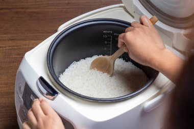 Kadın eli, elektrikli pilav fırınında pişirilen yasemin pilavını buharla kepçeliyor. Tayland Jasmine pirinci..