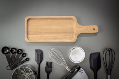 Fırın geçmişi. Ekmek kesme tahtası, ölçüm kaşığı, Paslanmaz çelik un süzgeci, Spatula, Gıda işlemcisi, Pasta fırçası, Silikon çırpıcı, fırın tepsisi, pişirme kağıdı, gri arka planda. Üst görünüm.