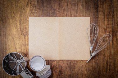 Fırın geçmişi. Kağıt ustası, paslanmaz çelik un süzgeci, fırın tepsisi, pişirme kağıdı, ahşap panelde silikon çırpıcı..