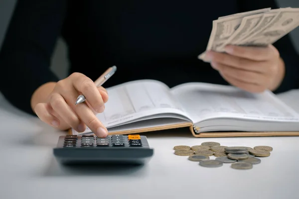Woman using calculator with pen in her hand and hold dollar bill for calculating financial expense at home office, financial accounting calculate money payments manage expenses.