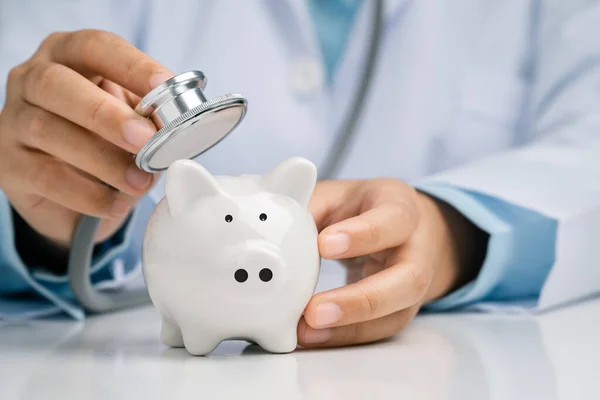 Doktor, kumbara mali kontrolünü kontrol etmek için steteskop kullanıyor, finansal durumun finansal sürdürülebilirliğini konsept olarak kontrol ediyor..