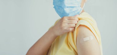 Yüz maskesi takan ve aşılanmış kolunu gösteren bir insan. Aşı, önerilen aşı konsepti.