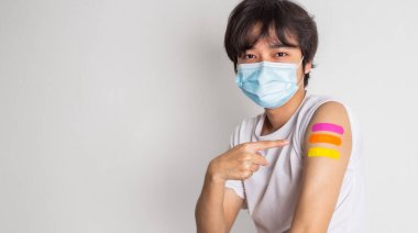 Asian man wearing face mask with a smile on his face showing his vaccinated arm. fight against virus covid-19 coronavirus, Vaccination and immunization. vaccine booster concept.