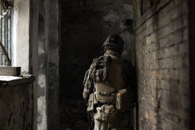 Eski, terk edilmiş bir koridorda, Amerikan askeri üniformalı bir adam elinde silahla hava yumuşaklığında bir spor oyunu oynuyor.