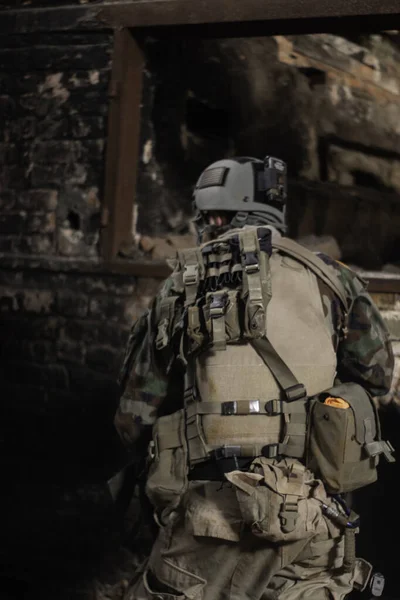 軍の制服を着た男が老朽化した建物の古い壁の背景に背を向けて立ってるエアソフトスポーツゲーム軍のシミュレーション — ストック写真
