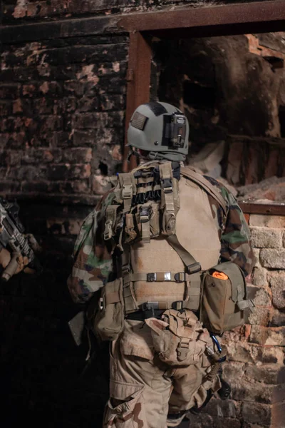 軍の制服を着た男が老朽化した建物の古い壁の背景に背を向けて立ってるエアソフトスポーツゲーム軍のシミュレーション — ストック写真