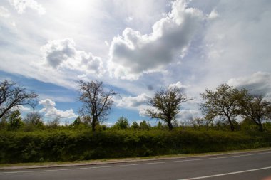 Yol kenarı ve güzel bulutlu gökyüzü araba penceresinden hareket ediyor.