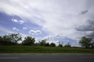 Yol kenarı ve güzel bulutlu gökyüzü araba penceresinden hareket ediyor.