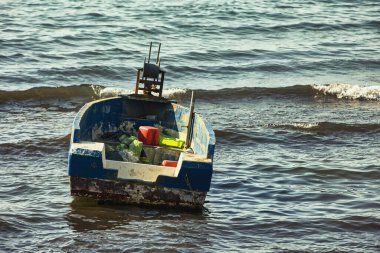 Arnavutluk 'un Vlor kentinde kıyıya yakın küçük eski bir balıkçı teknesi yüzüyor. Tekne teçhizat, plastik kaplar ve ağlarla dolu. Sıcak yaz ışığı altında sakin denizde yavaşça sallanıyorlar. 17.08.25.
