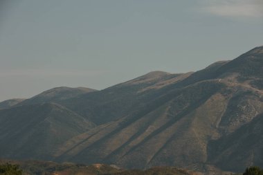 Arnavutluk 'un Vlor kenti yakınlarındaki dağ manzarası 17.08.25' te ele geçirildi. Yumuşak öğleden sonra ışığı kıvrımlı çıkıntıları ve yumuşak yamaçları vurgular.