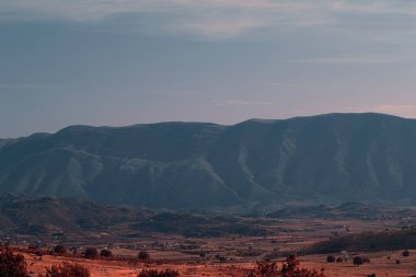 Arnavutluk 'un Vlor kenti yakınlarındaki dağ manzarası 17.08.25' te ele geçirildi. Yumuşak öğleden sonra ışığı kıvrımlı çıkıntıları ve yumuşak yamaçları vurgular.