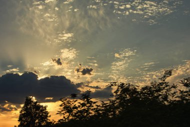 Karanlık dağ siluetlerinin üzerinde turuncu ve kırmızı tonlarda parlayan katmanlı bulutlarla dramatik, ateşli günbatımı, Ağustos 2025 'te yakalandı.