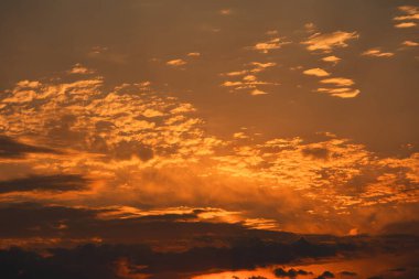 Karanlık dağ siluetlerinin üzerinde turuncu ve kırmızı tonlarda parlayan katmanlı bulutlarla dramatik, ateşli günbatımı, Ağustos 2025 'te yakalandı.