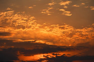 Karanlık dağ siluetlerinin üzerinde turuncu ve kırmızı tonlarda parlayan katmanlı bulutlarla dramatik, ateşli günbatımı, Ağustos 2025 'te yakalandı.