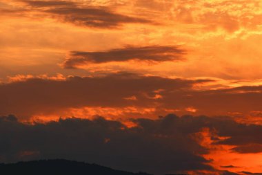 Karanlık dağ siluetlerinin üzerinde turuncu ve kırmızı tonlarda parlayan katmanlı bulutlarla dramatik, ateşli günbatımı, Ağustos 2025 'te yakalandı.