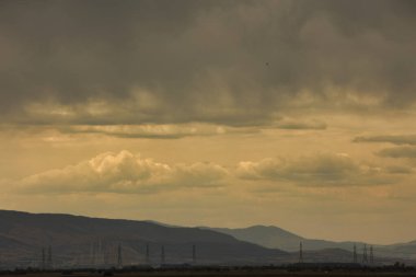 2025 Ağustosunun dramatik fırtınalı bulutları uzak dağların ve kırsal alandaki elektrik hatlarının üzerinde asılı..