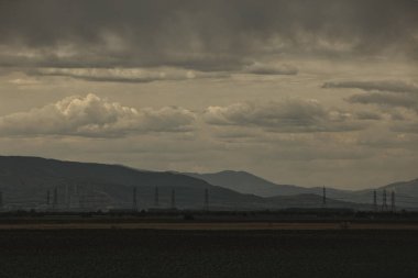 2025 Ağustosunun dramatik fırtınalı bulutları uzak dağların ve kırsal alandaki elektrik hatlarının üzerinde asılı..