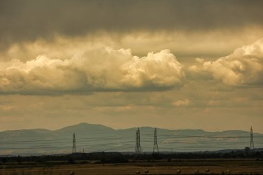 2025 Ağustosunun dramatik fırtınalı bulutları uzak dağların ve kırsal alandaki elektrik hatlarının üzerinde asılı..