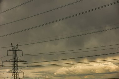 Yüksek voltajlı bir güç iletim kulesi dramatik, fırtınalı bir gökyüzüne karşı duruyor..