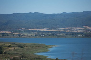 Berrak bir gökyüzü altında sakin bir mavi denizin üzerinde yükselen dağ sırası minimalist bir kıyı manzarası oluşturuyor. 29 Ağustos 2025 'te sakin doğal manzara.