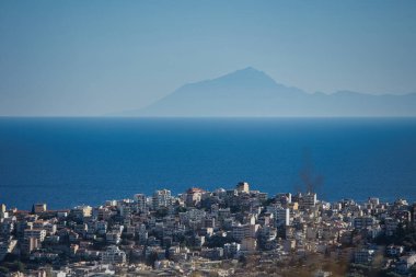Kıyı şehri, açık bir Ağustos 2025 'te uzak dağların sislenerek kaybolduğu derin mavi bir denize bakıyor..