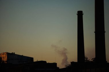 Endüstriyel bacalar dramatik bir günbatımı gökyüzüne karşı siluetlendi, Ağustos 2025 'te yoldan çekilen sıcak altın ışık, doğa ve kentsel altyapı arasında güçlü bir kontrast oluşturdu..