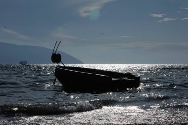 Vlor, Arnavutluk Ağustos 2025 Dağlık bir sahil şeridi ve sıcak akşam ışığı altında görünen küçük bir tekne ile kumlu kıyıya yumuşak dalgalar vuruyor.
