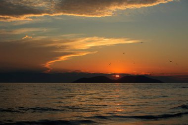 Altın gün batımı ışığı, 24 Ağustos 2025 'te Arnavutluk' un Vlora kentindeki yumuşak deniz dalgalarını yansıtarak yumuşak dalgalar ve uzak dağ siluetleriyle sıcak ve sakin bir kıyı atmosferi yaratıyor..