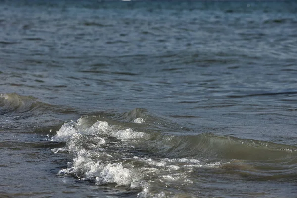 Arnavutluk 'un Vlora kenti Ağustos 2025' te kıyı kenti ve arka planda görünen yeşil Vlora dağlarıyla birlikte kıyıya doğru yumuşak dalgalar akmaktadır. Sahne, açık bir yaz gününde denizin sakin hareketini yakalar..