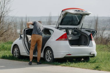 Adam arabasını kontrol ediyor. Beyaz araba yolu kenarı.