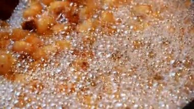 Making of crispy pork cracklings on pan in SLOW MOTION HD VIDEO. Fried pieces of pork skin floating in lard and foam and shuffling with ladle. Close-up.