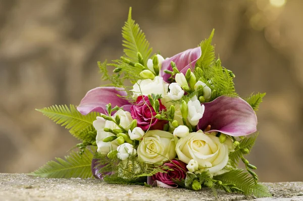 Bridal bouquet laying on stone block. Beautiful romantic white and magenta wedding flowers with copy space and blurred background. Close-up.