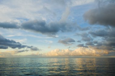 Karayip Denizi üzerinde gün batımı. Dalgalar ve bulutlarla derin okyanus manzarası. Rahatlatıcı deniz manzarası, tropikal sular. Mavi denizler ve batan güneşin altın yansıması uzak bir ufukla ayrılmış..