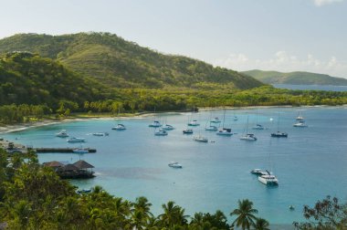 Gemiler tropik körfezde demirliyor. Mavi deniz suyunda bir sürü küçük yat, yeşil tepeler ve arka planda mavi gökyüzü. Britanya Körfezi 'nin havadan görünüşü, Mustique adası. Karayip yaşam tarzı temaları.