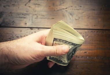 Tahta masa arkasında 100 Amerikan banknotuyla el ele tutuşmak. Yüz dolarlık banknotlar, kağıt para birimi..