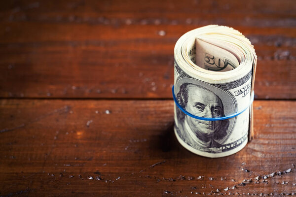 Рулон денег с резиной на деревянном столе - сто американских банкнот с портретом президента Франклина. Денежные средства стодолларовые купюры, бумажная валюта фон.