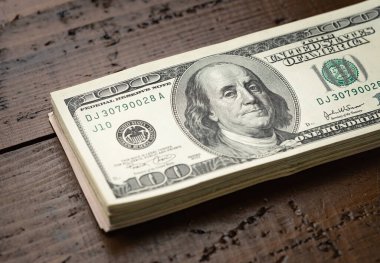 Bir para yığını, üzerinde Başkan Franklin 'in portresi olan 100 banknotu ahşap masa arkasına yığdı. Yüz dolarlık banknotlar, kağıt para birimi..