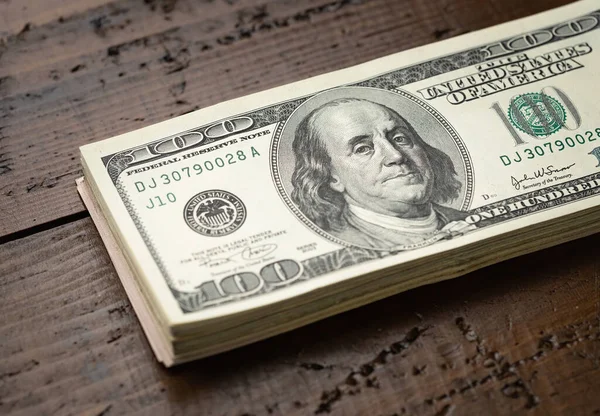 Bir para yığını, üzerinde Başkan Franklin 'in portresi olan 100 banknotu ahşap masa arkasına yığdı. Yüz dolarlık banknotlar, kağıt para birimi..