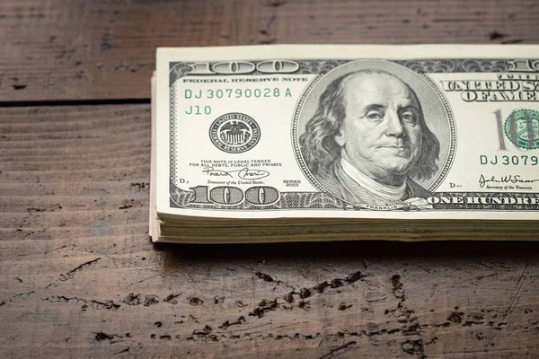 Bir para yığını, üzerinde Başkan Franklin 'in portresi olan 100 banknotu ahşap masa arkasına yığdı. Yüz dolarlık banknotlar, kağıt para birimi..