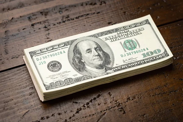 Bir para yığını, üzerinde Başkan Franklin 'in portresi olan 100 banknotu ahşap masa arkasına yığdı. Yüz dolarlık banknotlar, kağıt para birimi..