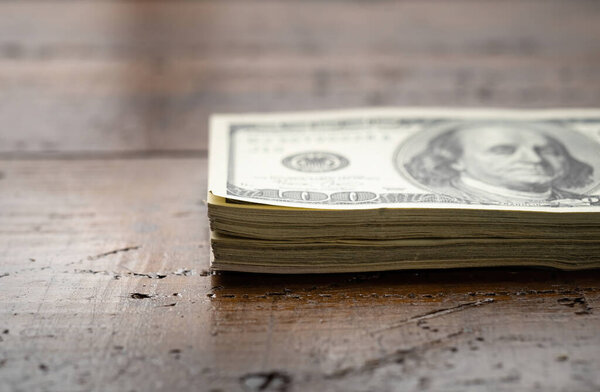 A money pile of stacked one hundred US banknotes with president Franklin portrait over wooden table background. Cash of hundred dollar bills, paper money currency.