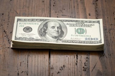 Bir para yığını, üzerinde Başkan Franklin 'in portresi olan 100 banknotu ahşap masa arkasına yığdı. Yüz dolarlık banknotlar, kağıt para birimi..