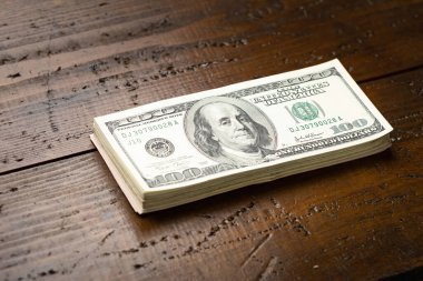Bir para yığını, üzerinde Başkan Franklin 'in portresi olan 100 banknotu ahşap masa arkasına yığdı. Yüz dolarlık banknotlar, kağıt para birimi..