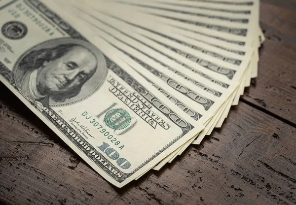 A money pile of fan stacked one hundred US banknotes with president Franklin portrait over wooden table background. Cash of hundred dollar bills, paper money currency.