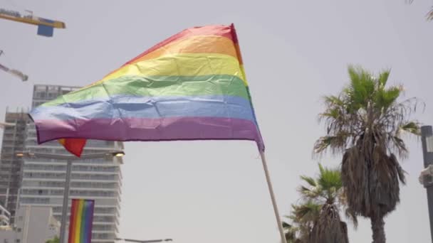Pride Rainbow Flag vinkar i vinden. Låg vinkel skott av hbt färgglada medvetenhet symbol flagga med himmel, stadstorn och kranar i bakgrunden. — Stockvideo
