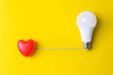 Sarı arka planda ampulü olan kırmızı kalp. Bu fikrin kökeni Sevgililer Günü 'nüz kutlu olsun. Aşk, düğün. Boşluğu kopyala