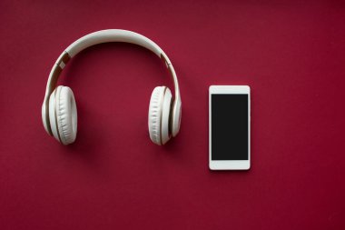 Beyaz Ekran ve Kırmızı Arkaplanda Beyaz Kulaklıklı Akıllı Telefon. Üst Manzara. Boşluğu kopyala.