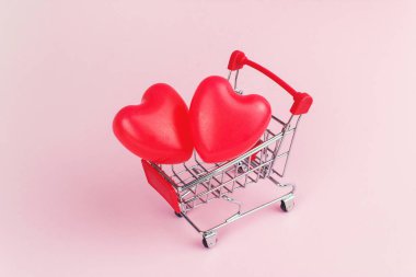Kırmızı kalp küçük alışveriş arabasında pembe arka planda, alışveriş ve aşk konseptinde şekilleniyor..